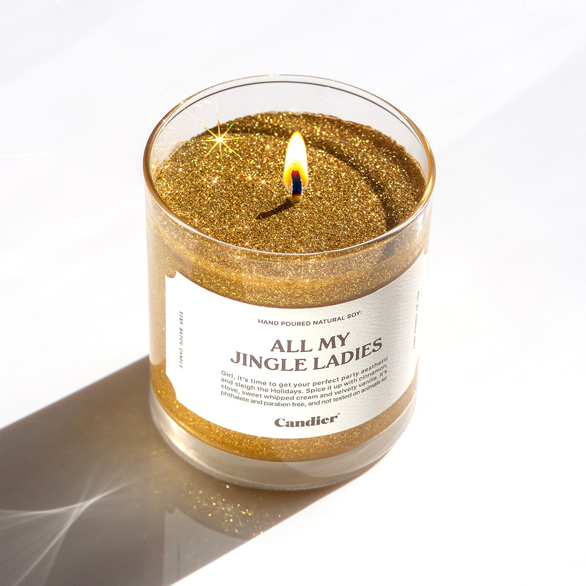 A lit shining sparkly gold Christmas themed scented candle with a label that reads ALL MY JINGLE LADIES by Candier