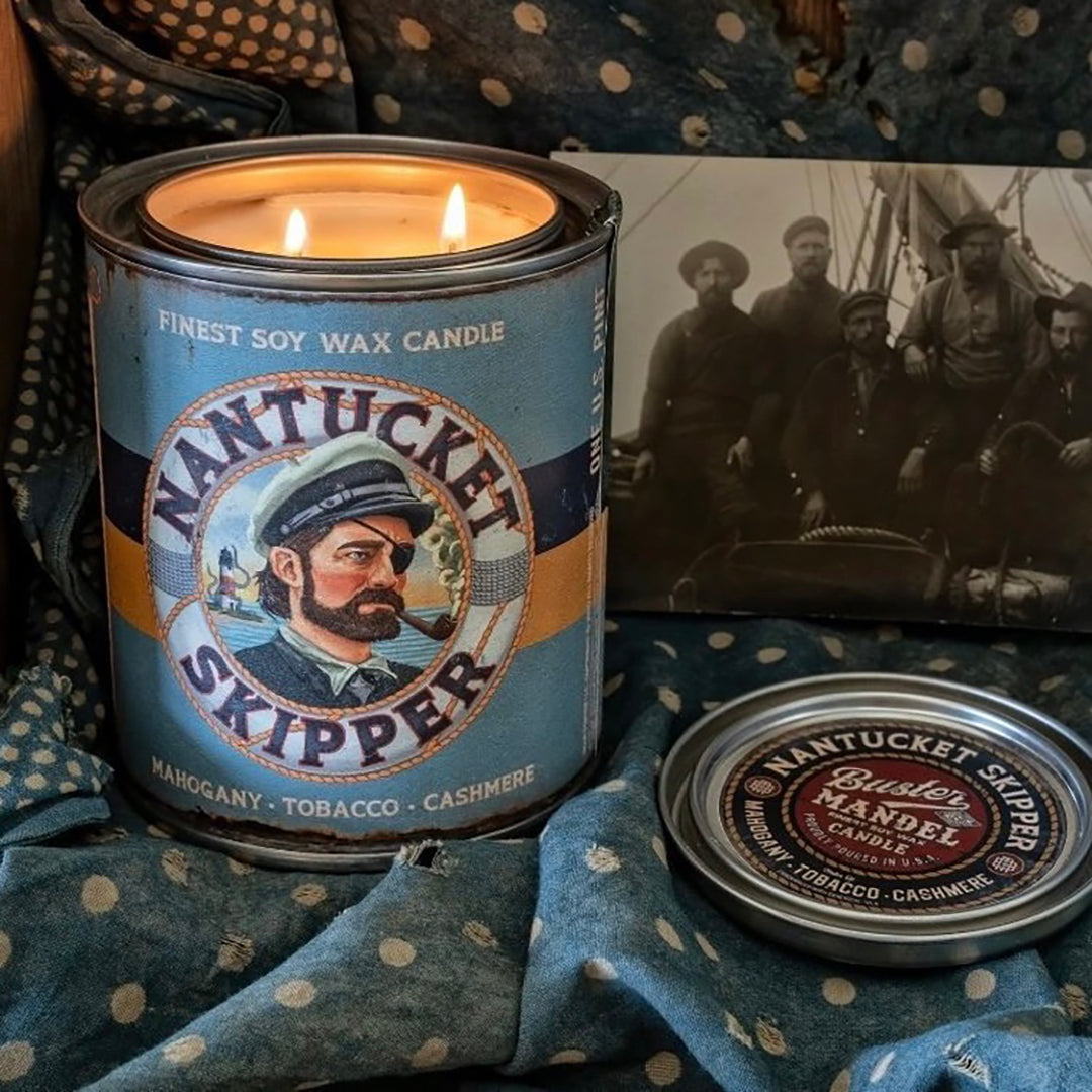 Nantucket Skipper Candle burning in a vintage maritime setting. A luxury masculine fragrance with mahogany, pipe tobacco, and warm cashmere notes