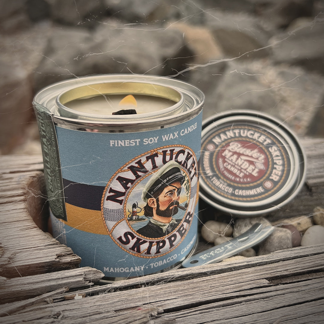 Nantucket Skipper Candle displayed on rustic driftwood. A bold, seafaring scent with mahogany, clove, and pipe tobacco. Dual wood wicks for a rugged burn