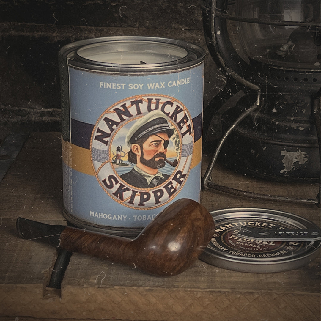 Nantucket Skipper Candle set with an old wooden pipe and lantern, evoking the scent of mahogany, cashmere, and rich pipe tobacco. Hand-poured in the USA