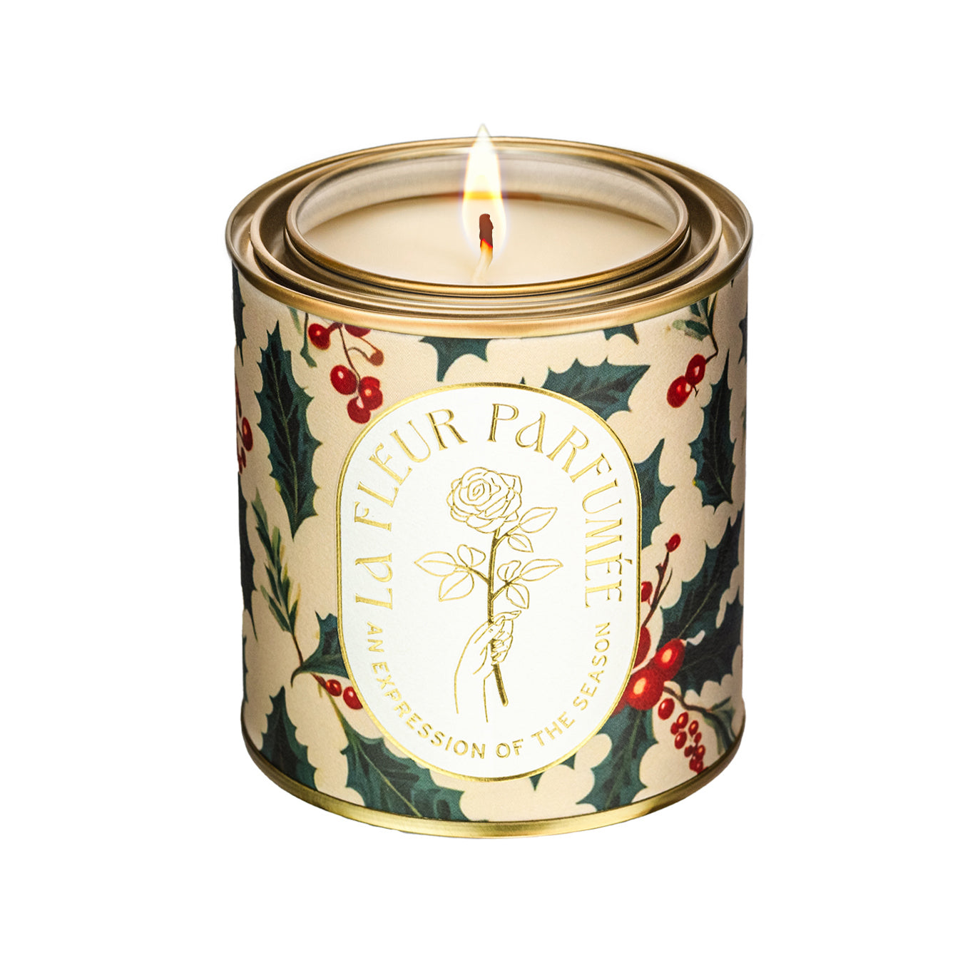 An elegant luxe lit gold-tone candle,  wrapped in artwork of a festive pattern showcasing classic holly leaves in deep green, accented by vibrant red berries. The cream-colored background contrasts beautifully with the rich, glossy leaves and clusters of berries, creating a lively and cheerful holiday atmosphere. The design evokes traditional Christmas decor, full of timeless seasonal charm and warmth