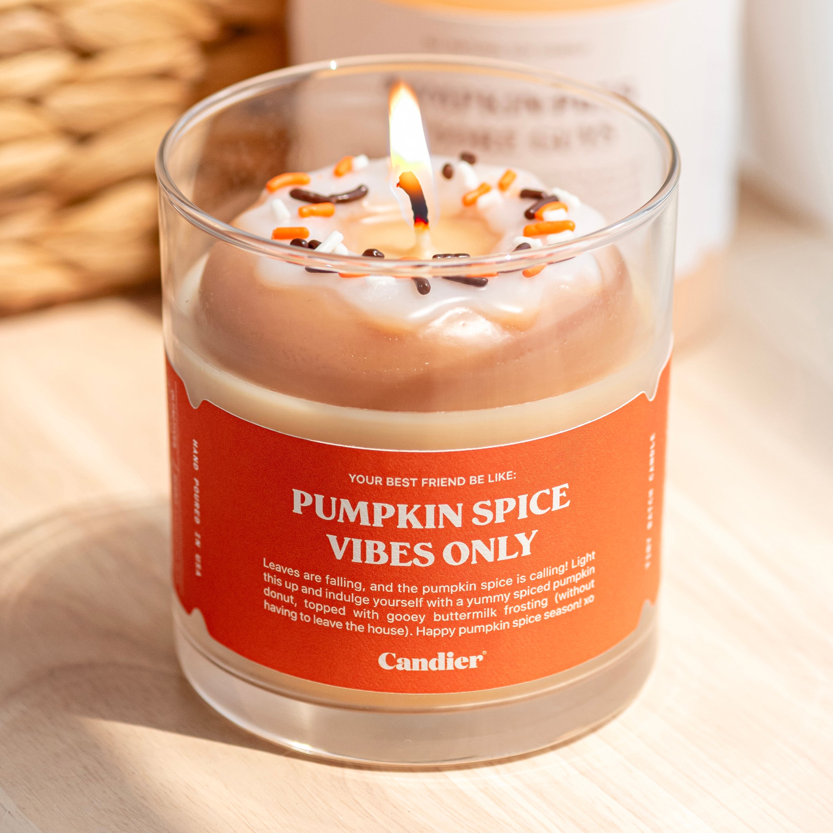 A cute lit fall scented candle with a wax glazed donut on top and a label that reads Pumpkin Spice Vibes Only