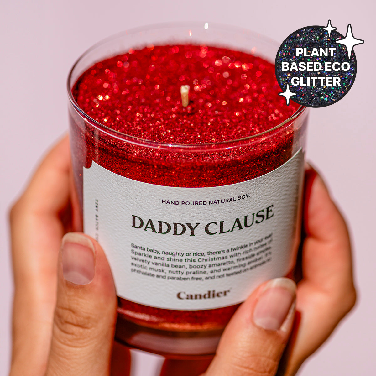 A woman holding a festive Christmas red scented candle with sparkling glitter and a label that reads Daddy Clause by Candier, with a badge that says Plant Based Eco Glitter