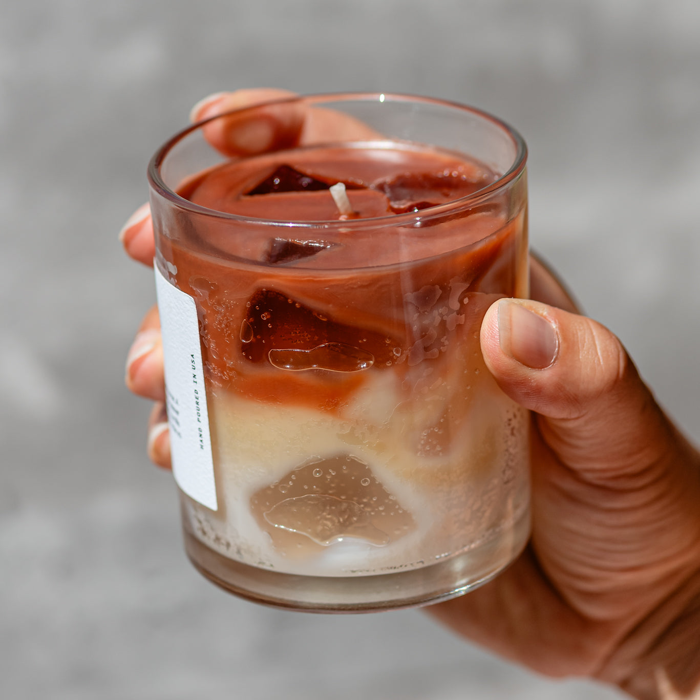 Ice coffee espresso latte inspired candle held in a woman's hand, showing ice cube effect in candle