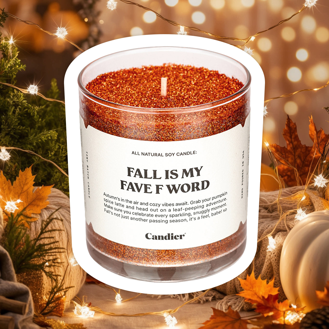 A sparkling autumn colored candle with plant based glitter and a label that reads Fall Is My Fave F Word, with a cozy background of fall decor, autumn leaves and festive pumpkins