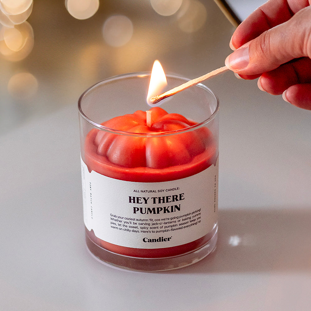 A cute pumpkin shaped candle being lit with a match