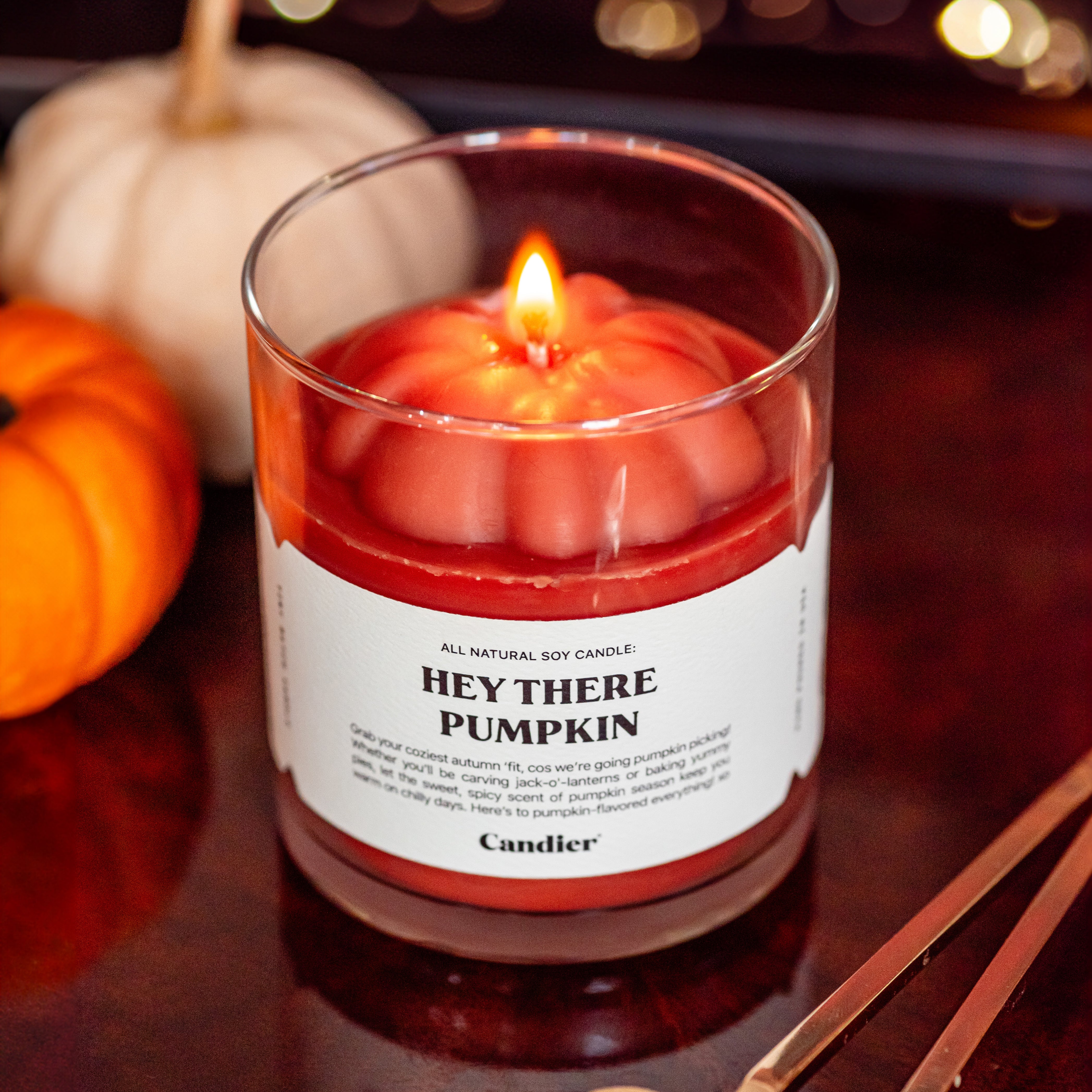 A lit cute pumpkin shaped candle in a cozy fall decorated room