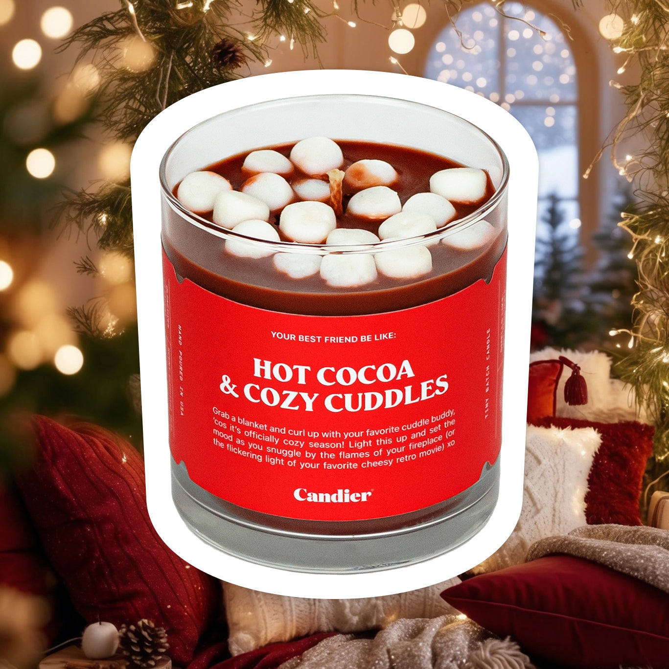 A cute chocolate colored candle topped with mini wax marshmallows and a red labek that reads Hot Cocoa and Cozy Cuddles, with a cozy background of twinkly lights, plush farmhouse decor and cozy blankets