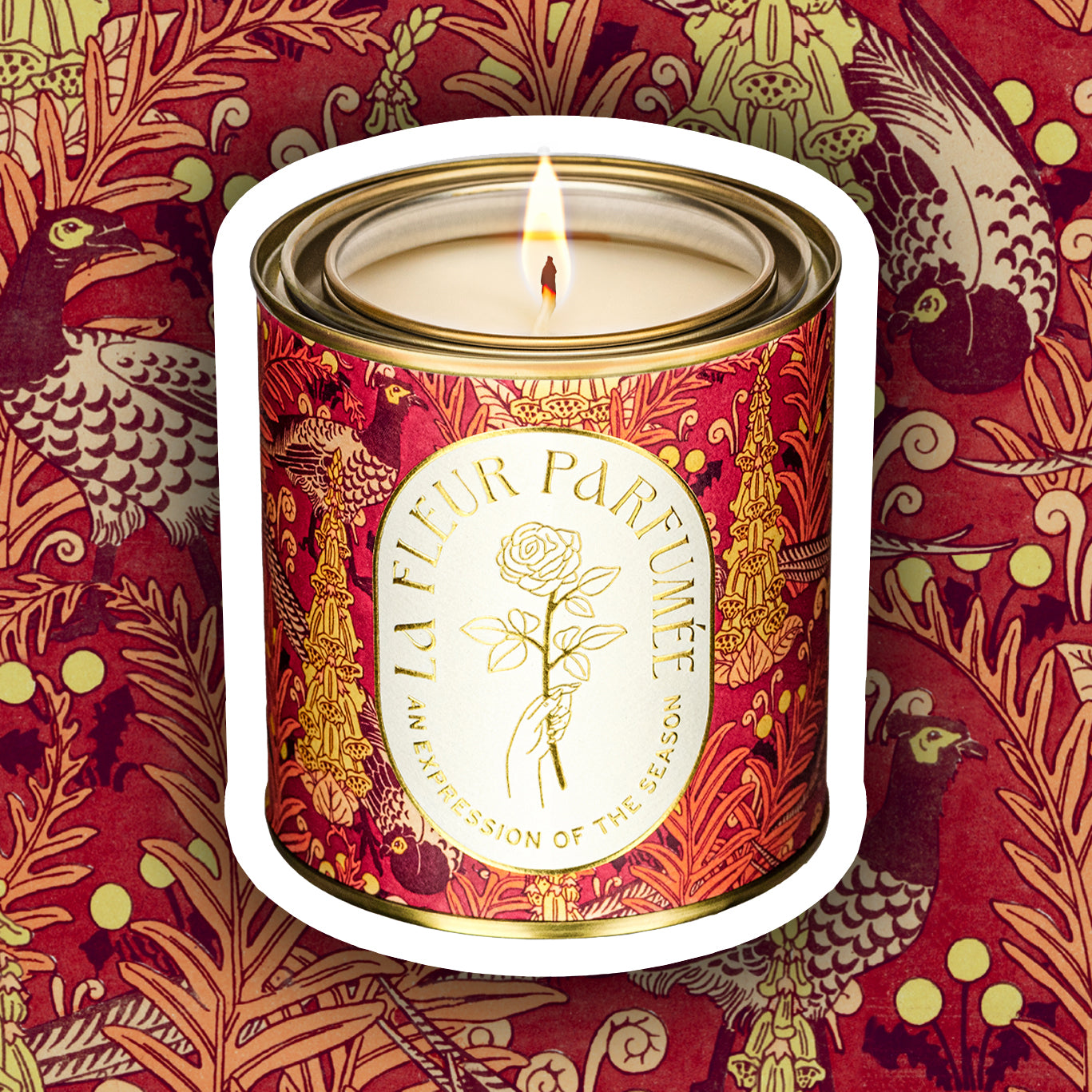 A luxury scented candle with a bold seasonal, fall, thanksgiving themed pattern, with a crisp white label and gold writing that reads LA FLEUR PARFUMÉE: An Expression of the Season, and an illustration of a hand holding an elegant rose by the stem.