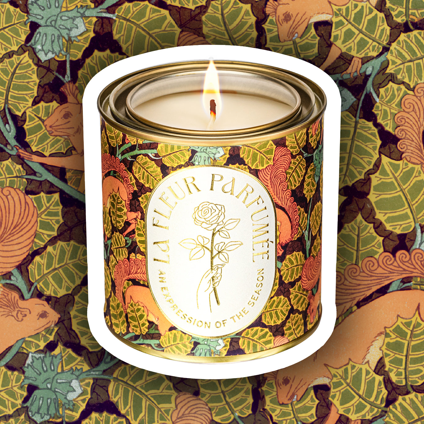 A luxury scented candle with a bold seasonal, fall, thanksgiving themed pattern, with a crisp white label and gold writing that reads LA FLEUR PARFUMÉE: An Expression of the Season, and an illustration of a hand holding an elegant rose by the stem.