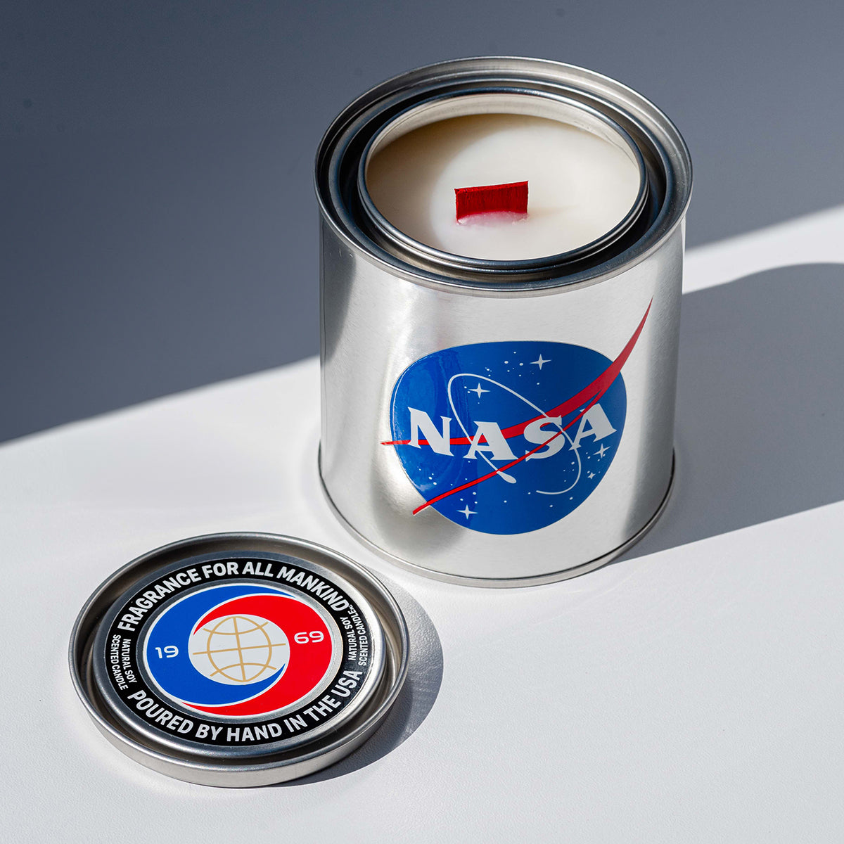 The BREVRN NASA 1969 candle with its lid removed, revealing the natural soy wax and signature red wood wick for an elevated burning experience.