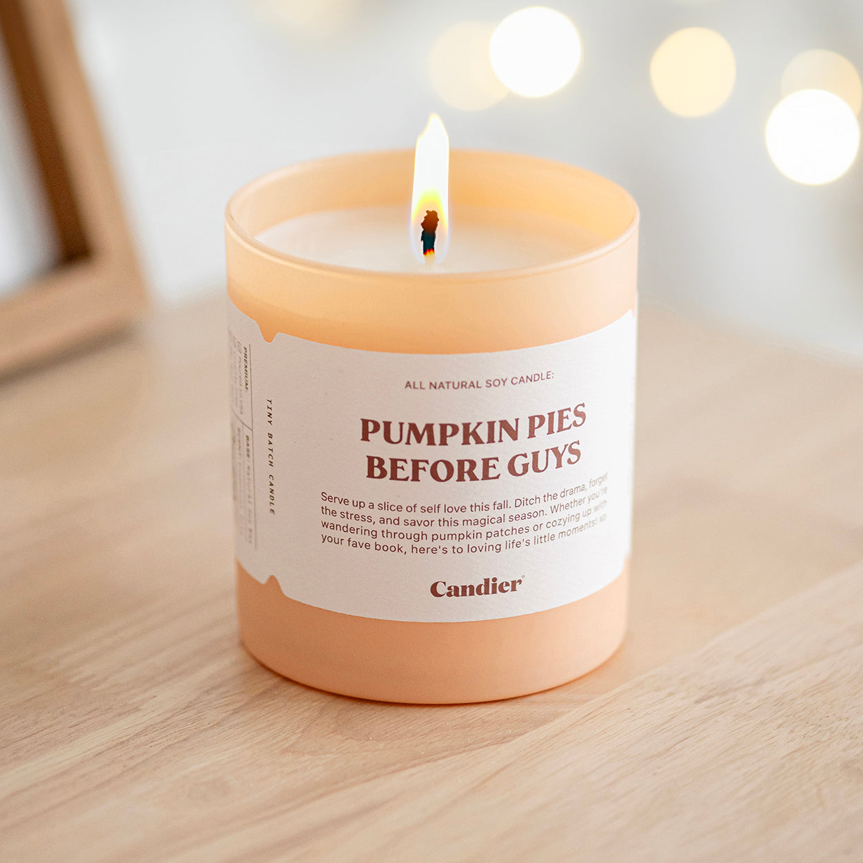 A lit cute luxury fall scented candle with a label that reads Pumpkin Pies Before Guys