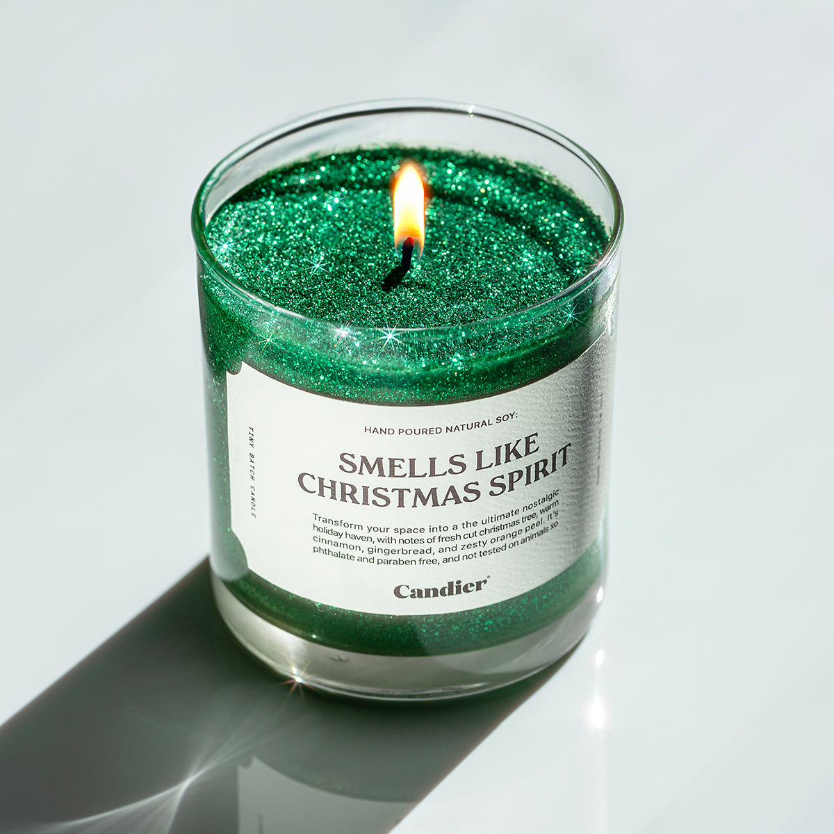 A lit festive Christmas green glitter scented candle with a label that reads SMELLS LIKE CHRISTMAS SPIRIT by Candier