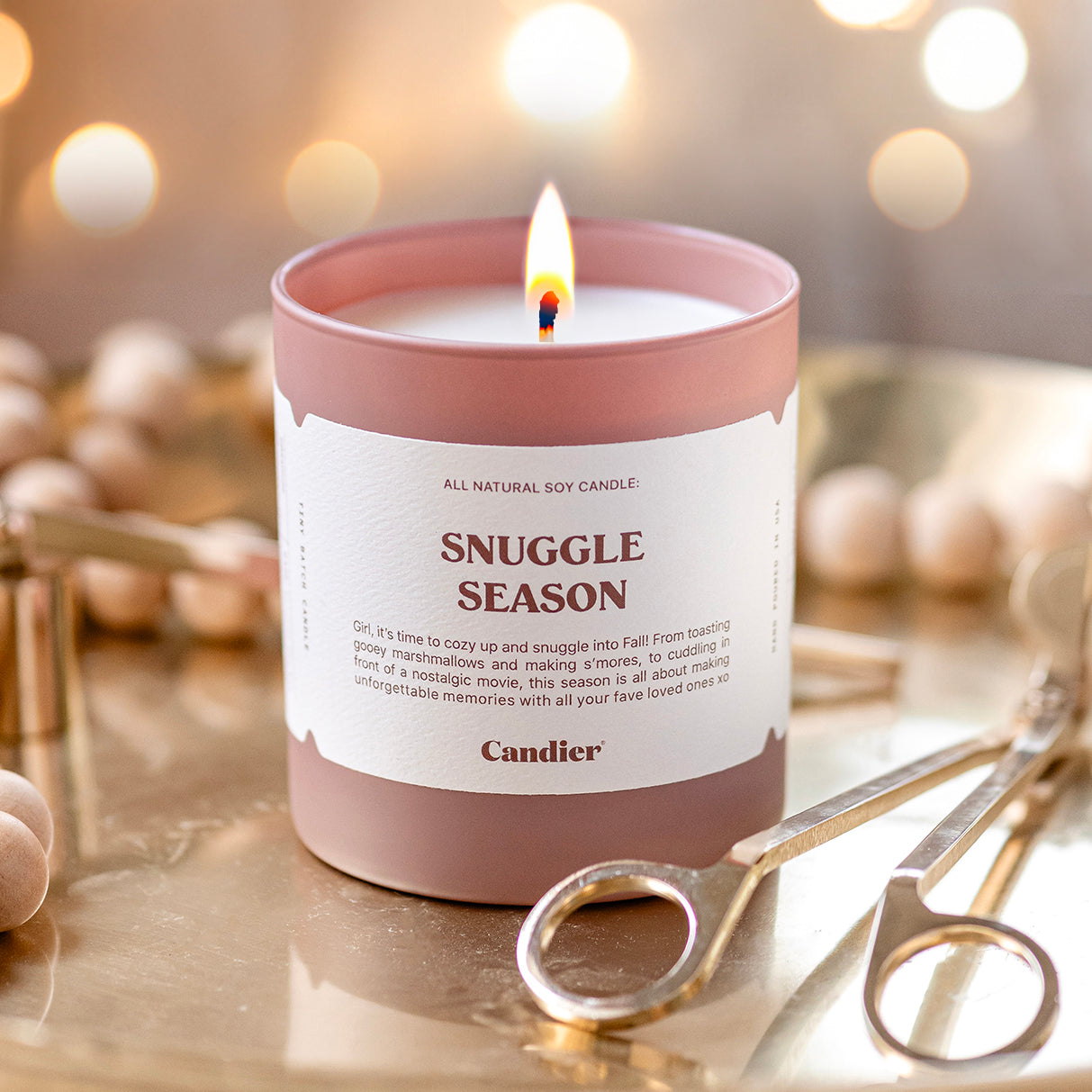 a lit luxury scented candle with a message that reads Snuggle Season 