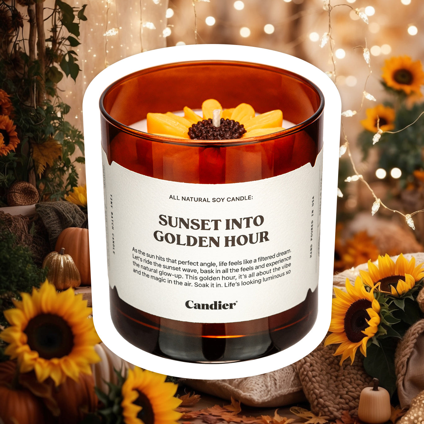 An amber colored candle with a molded wax sunflower in top and a label that reads Sunset Into Golden Hour by Candier, with a cozy background of autumn themed decor