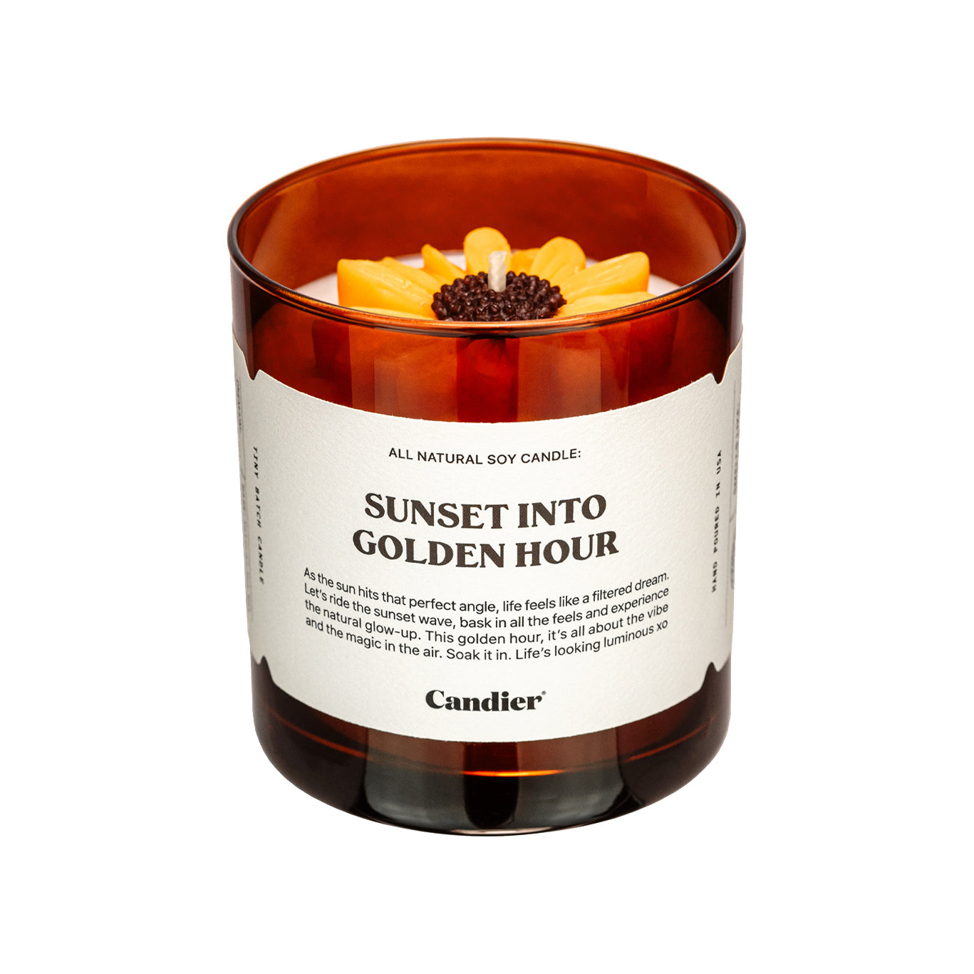 An amber colored candle with a molded wax sunflower in top and a label that reads Sunset Into Golden Hour by Candier