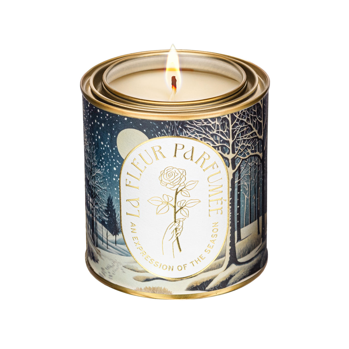 An elegant luxe lit gold-tone candle,  wrapped in artwork of a peaceful winter night scene illuminated by the soft glow of the moon, with snow gently falling over a quiet forest. Bare trees stretch upward, their branches dusted with light snow, while soft snowdrifts blanket the ground. Footprints trail off into the distance, adding a sense of wonder. The composition evokes a serene winter’s eve.