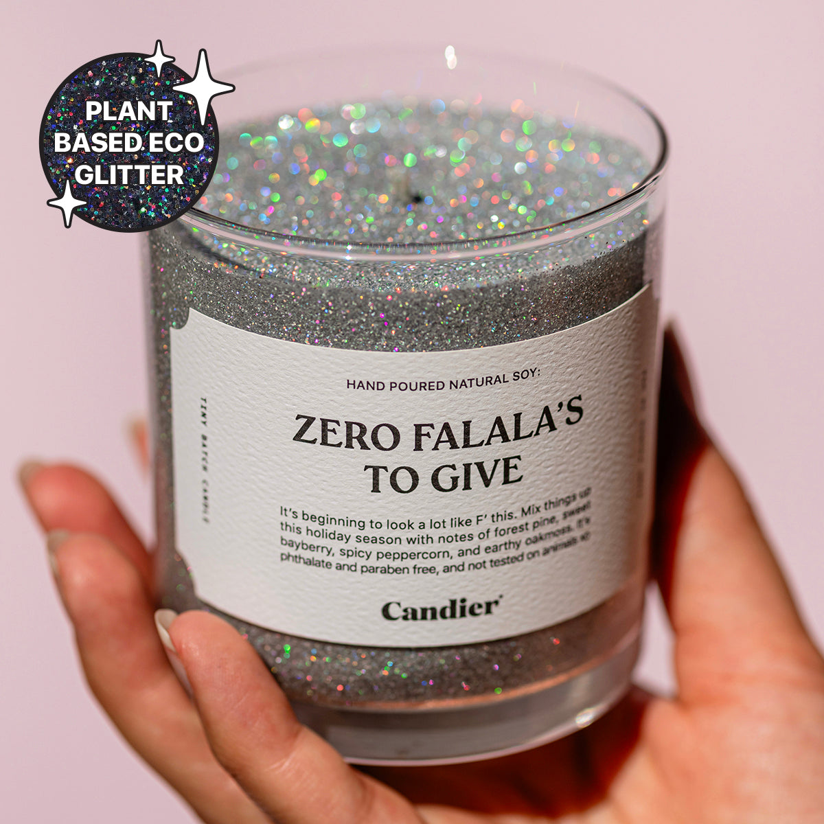 A woman holding a sparkling holiday themed candle with a label that read Zero Falala's to Give by Candier and a badge that says Plant Based Eco Glitter