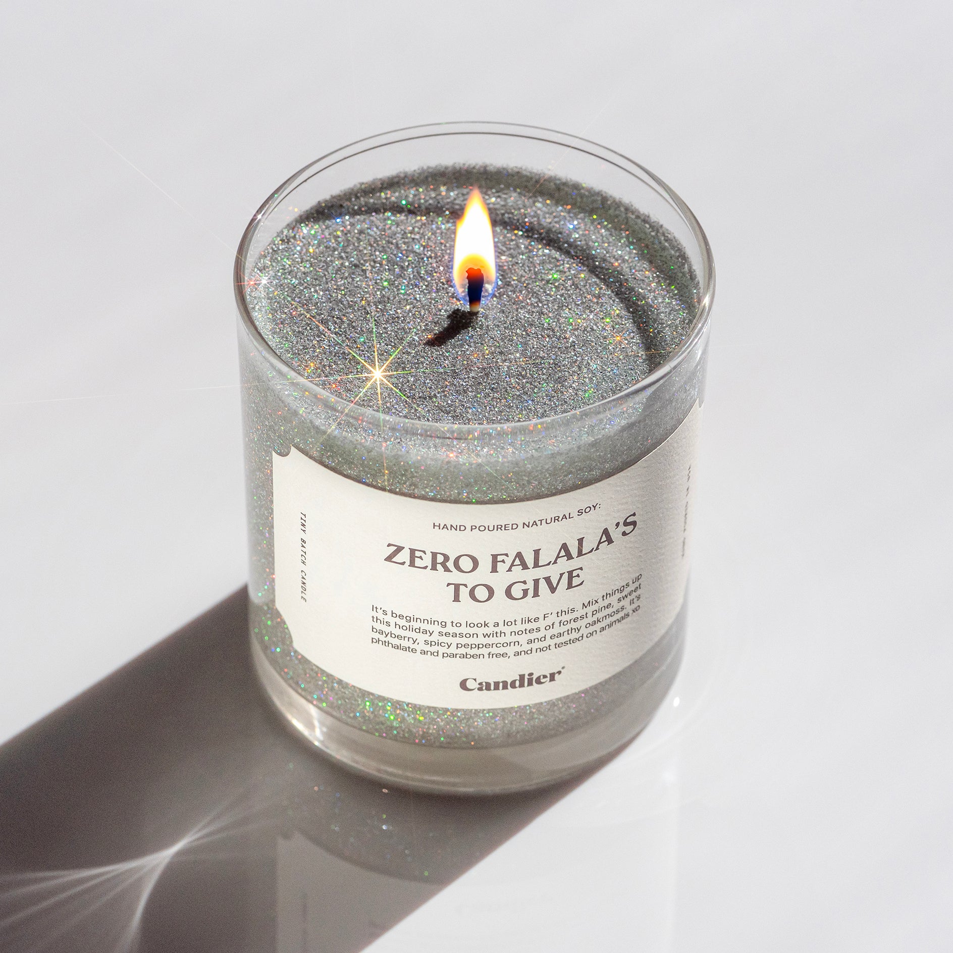 A lit sparkling Christmas themed candle with a label that read Zero Falala's to Give by Candier, topped with plant based eco glitter