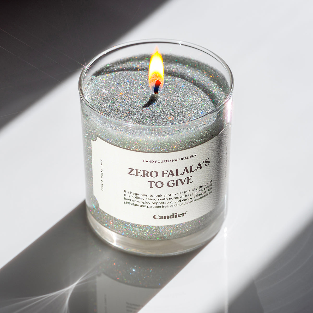 A lit sparkling holiday themed candle with a label that read Zero Falala's to Give by Candier and a badge that says Plant Based Eco Glitter